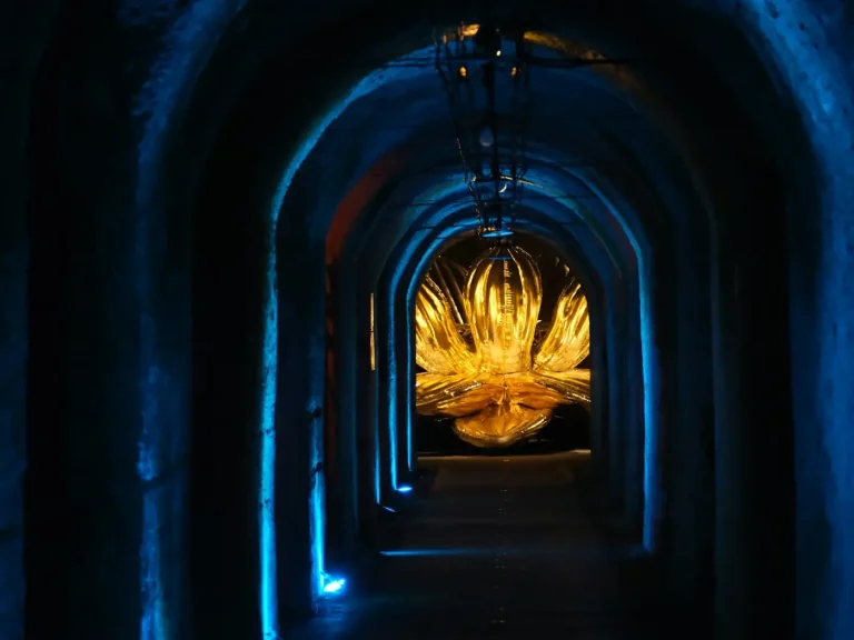 Galerie voûtée creusée dans la craie, sous la colline Saint-Nicaise à Reims, éclairée de bleu, avec une œuvre lumineuse au fond