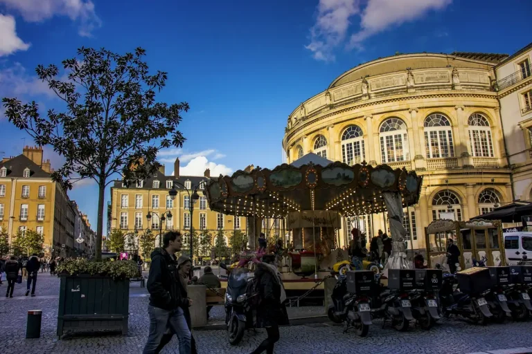 Passants autour du carrousel, devant la façade arrondie de l’Opéra de Rennes, place de la Mairie