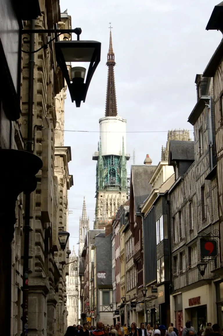 La flèche de la cathédrale Notre-Dame de Rouen au bout d’une rue commerçante du centre historique, animée de passants