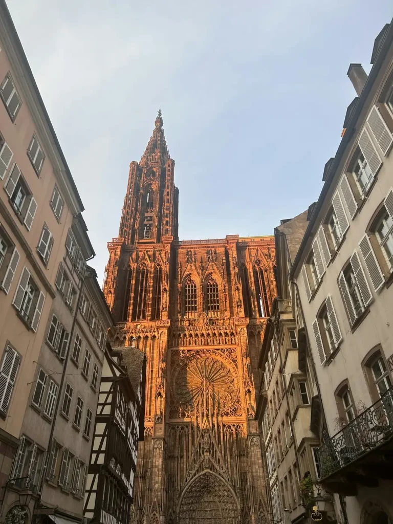 La façade de la cathédrale Notre-Dame de Strasbourg au bout d’une rue du centre historique, au soleil couchant