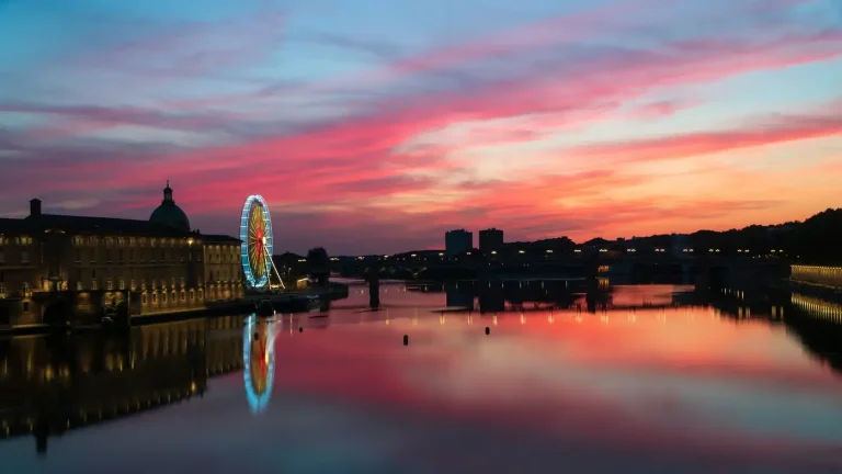 La Garonne au coucher du soleil, à Toulouse : le dôme de La Grave et une grande roue illuminée se reflètent dans l’eau