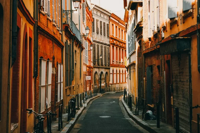 Une rue étroite du centre historique de Toulouse, entre des façades de brique et d’enduit ocre aux volets clairs