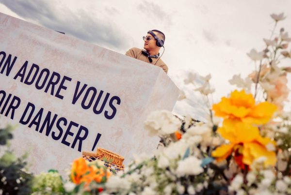 DJ derrière une cabine ornée du message « On adore vous voir danser ! » et entourée de fleurs, à la cocktail party Dior organisée par Weevup sur un rooftop