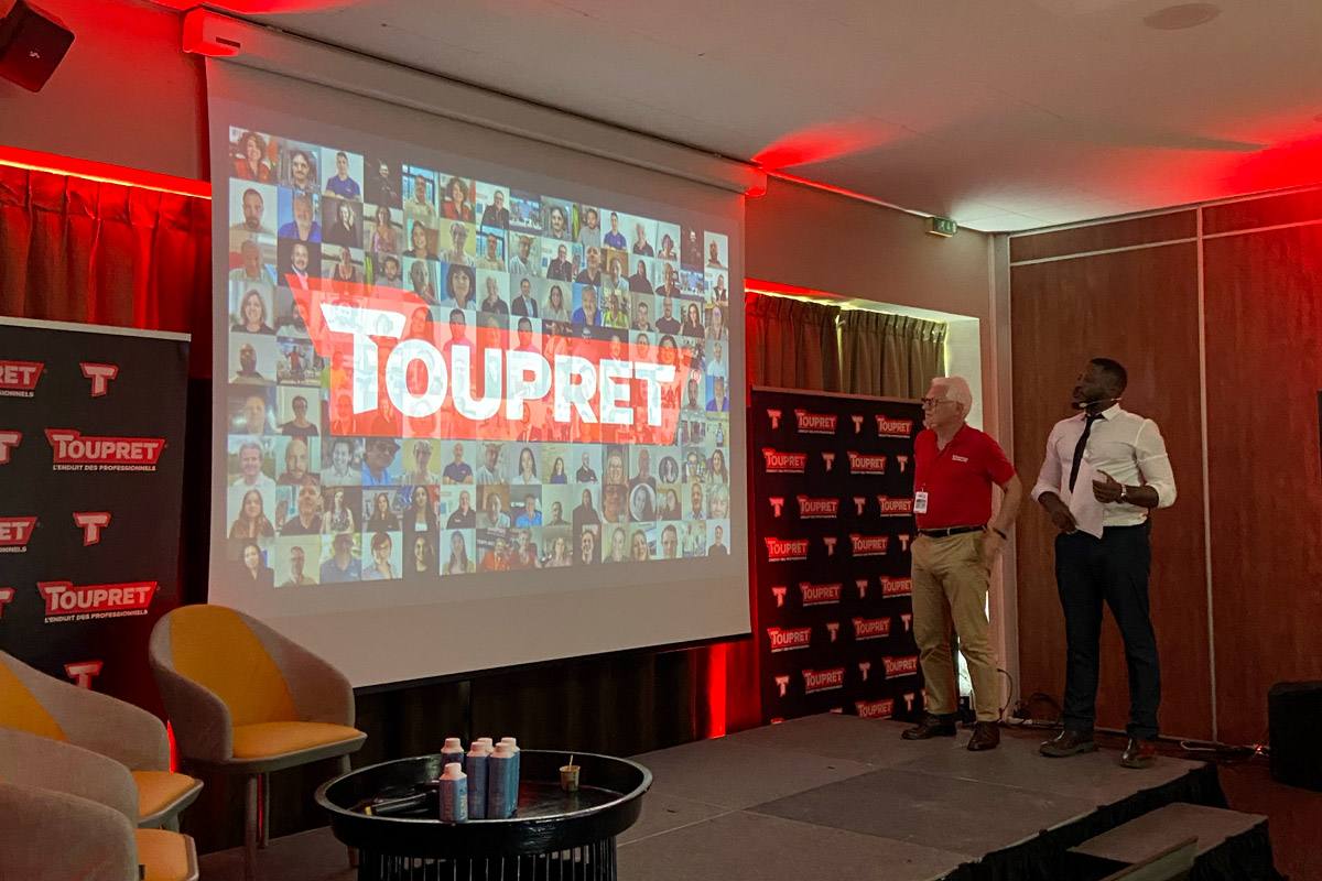 Deux intervenants sur scène devant un écran affichant le logo Toupret et la mosaïque des collaborateurs connectés à distance, pendant la convention hybride Cap 30 Connect organisée par Weevup